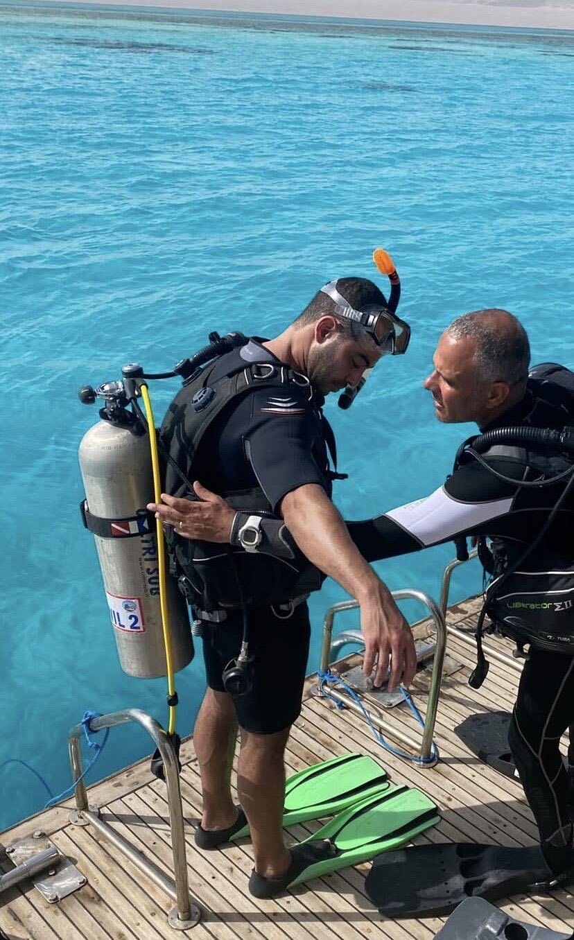 An instructor checks a diver's equipment on the boat's dive platform before the diver steps into the water.