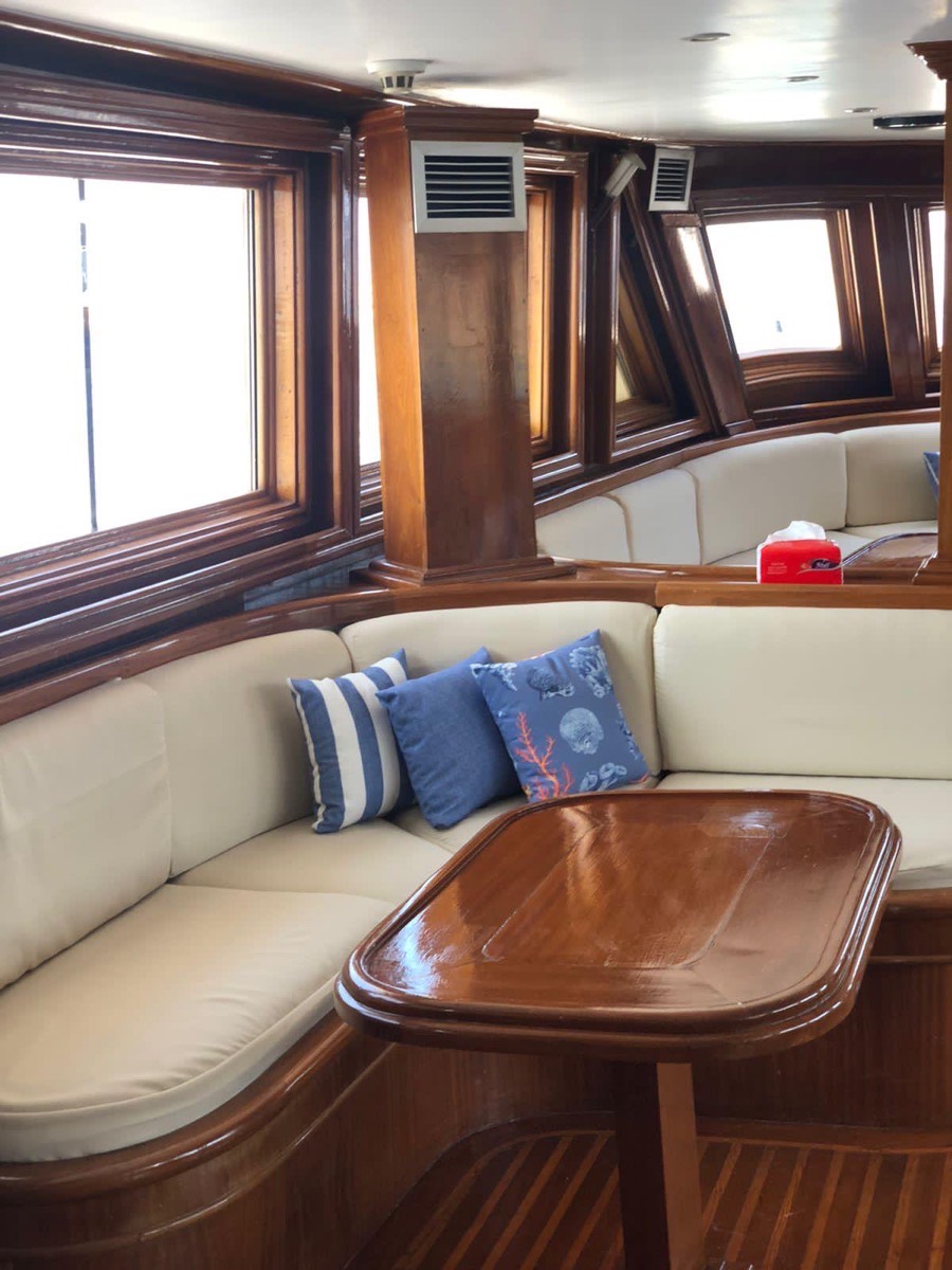 The saloon, with polished wooden window frames, cream built-in seating, blue cushions and a varnished table.