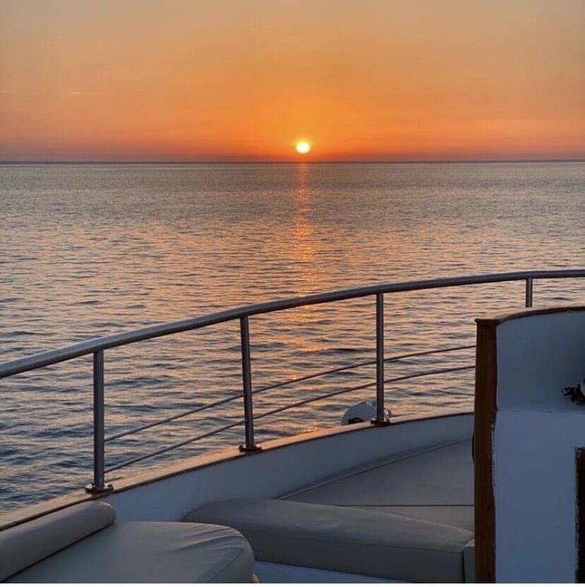 The sun setting over calm sea, seen past the bow rail.
